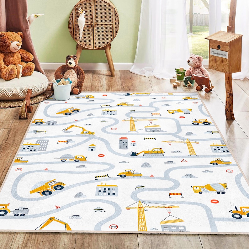 May include: A white play mat with a road and construction vehicle design. The mat features a winding gray road with yellow construction vehicles, buildings, and construction cranes. The design includes stop signs and other road details.