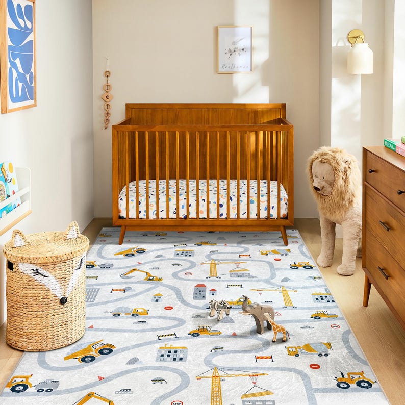 May include: A nursery scene featuring a wooden crib, a road-themed rug with construction vehicles, and a woven basket. The rug has a light gray background with a road design and yellow construction vehicles. A stuffed lion stands near a wooden dresser.
