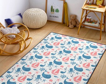 May include: A white rug with a blue and pink nautical pattern featuring whales, anchors, and starfish. The rug has a dark blue border.