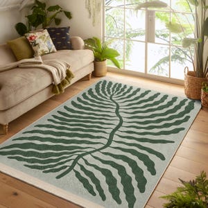 May include: A green and white area rug with a large fern leaf design. The rug has a light grey background with a dark green fern leaf pattern.