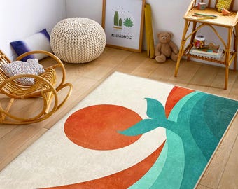 May include: A rectangular rug with a cream background features a large orange circle and a teal whale tail design. Teal and orange curved lines create a wave effect. The rug is placed on a wooden floor.