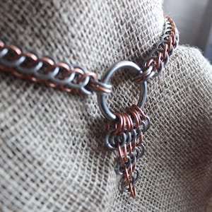 Może przedstawiać: Naszyjnik z łańcucha kolczastego w kolorze srebrnym i miedzianym z dużym srebrnym pierścieniem i wiszącym ozdobnym elementem z łańcucha kolczastego.