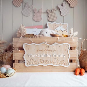 May include: A wooden crate with a personalised sign that reads "special delivery for The Griffiths Family". The crate is decorated with fairy lights and a garland of gingham bunny shapes. The crate is filled with gifts, including a stuffed bunny, a book, and a wooden egg.