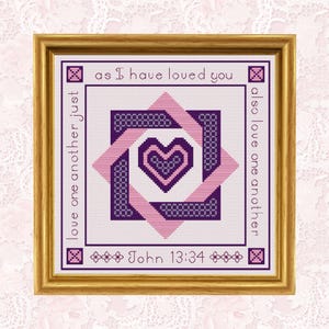 Puede incluir: Obra de arte de punto de cruz enmarcada con un marco dorado. El diseño presenta un corazón en tonos morados y rosas, rodeado de patrones geométricos y el texto "as I have loved you" y "love one another just". También se incluye el texto "John 13:34".