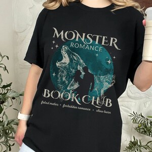 May include: Black t-shirt with a graphic design of a wolf couple with the text "Monster Romance Book Club" and the tagline "Fated Mates - Forbidden Romance - Slow Burn".