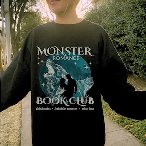 Puede incluir: Sudadera negra con un estampado gráfico de un lobo aullando a la luna. El texto "Monster Romance Book Club" está impreso en la sudadera. El texto "fated mates - forbidden romance - slow burn" está impreso debajo del gráfico.