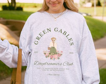May include: A gray sweatshirt with a green and white graphic print of a woman sitting on a bench with a book. The graphic also includes the text "Green Gables Daydreamers Club" and the dates "EST 1908".