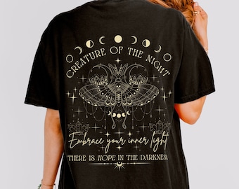May include: Black t-shirt with a gold graphic of a moth with moon phases and the text "Creature of the Night. Embrace your inner light. There is hope in the darkness."