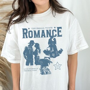 Comfort Colors Shirt in the Color white. Cowboy/Western Romance Book Shirt. Text:The small town romance, love stories of the real west, western love trails;.