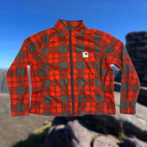 May include: Red and gray plaid fleece jacket with a zipper closure. The jacket has a small logo patch on the left chest.