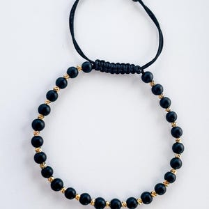Peut inclure: Bracelet en perles noires avec des accents dorés et une fermeture en cordon noir.