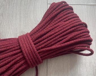 May include: A bundle of burgundy-colored rope, tightly coiled and secured with a wrapped section. The rope has a thick, textured appearance, suggesting it is made of a durable material. The color is a deep, rich shade of red, with a slight matte finish.