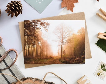 May include: A greeting card with a photograph of a misty forest path in autumn colors. The path leads into the distance, with trees on either side. The sun is shining through the trees, creating a warm glow.
