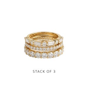Puede incluir: Un conjunto de tres anillos de oro con piedras transparentes. El anillo superior tiene piedras talla baguette y redondas, el central una hilera de piedras redondas pequeñas y el inferior una hilera de piedras redondas grandes. OCTONOV está grabado.