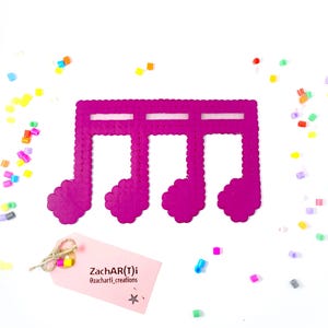 Puede incluir: Un diseño de nota musical rosa hecho con cuentas perler. El diseño presenta tres notas musicales conectadas por una barra. El diseño está sobre un fondo blanco.