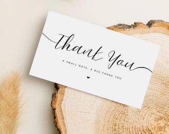 May include: A white card with the words "Thank You" in elegant black script. Below, smaller text reads "A small note, a big thank you," with a small heart. The card rests on a wooden surface.