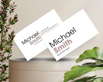 Puede incluir: Dos tarjetas de visita blancas con texto negro. La tarjeta superior tiene el nombre "Michael Smith" en negro y el título "Agente inmobiliario" en marrón. La tarjeta inferior tiene el mismo nombre y título, pero el nombre está en negro y el título en marrón. Las tarjetas están sobre una superficie blanca.