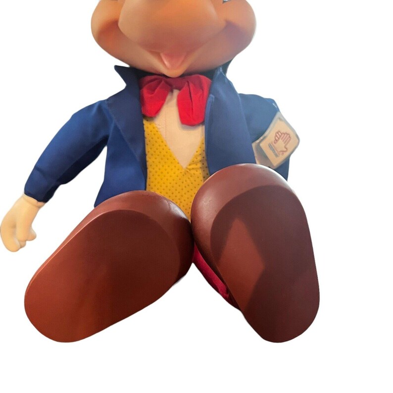 Peut inclure: Un jouet en peluche Mickey Mouse portant un costume bleu avec un gilet jaune, un n&oelig;ud papillon rouge et des chaussures marrons. Le jouet a une &eacute;tiquette sur son bras qui dit "Disney's Mickey Mouse".