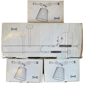 May include: A stack of IKEA boxes showing line drawings of lighting fixtures. The boxes depict various lamps, including a track lighting system and individual lamps with pleated shades. The IKEA logo is visible on each box.