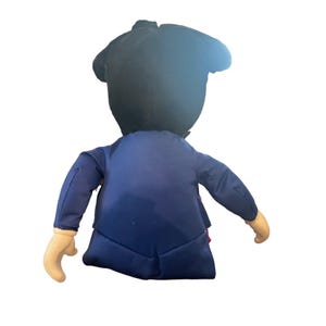 Peut inclure: Un jouet en peluche en forme de personne portant un costume bleu et un chapeau noir. Le jouet a un n&oelig;ud papillon rouge et une chemise blanche.