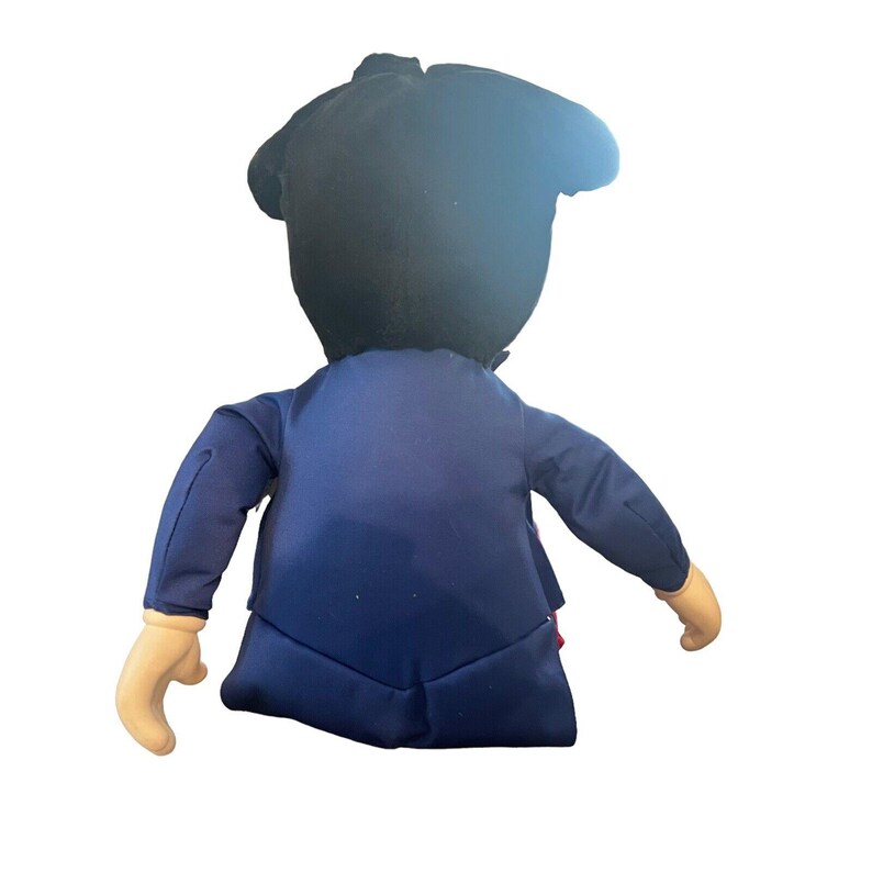 Peut inclure: Un jouet en peluche en forme de personne portant un costume bleu et un chapeau noir. Le jouet a un n&oelig;ud papillon rouge et une chemise blanche.