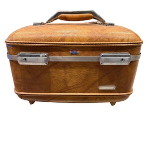 May include: A vintage brown suitcase with a textured exterior, silver metal accents, and a leather handle. The suitcase has a rectangular shape with rounded edges and small feet. A small emblem is visible on the front.