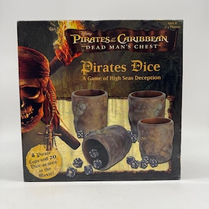 May include: A Pirates of the Caribbean Dead Man's Chest board game box featuring four brown textured dice cups and twenty black dice with white skull icons. The box displays a skull graphic, a flaming torch, and the text Pirates Dice.