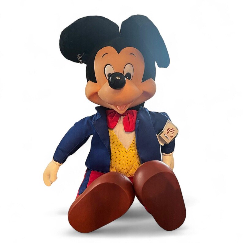 Peut inclure: Un grand jouet en peluche Mickey Mouse portant un costume bleu avec un n&oelig;ud papillon rouge et un gilet &agrave; pois jaunes. Le jouet a une ceinture ray&eacute;e rouge et bleue et des chaussures brunes.