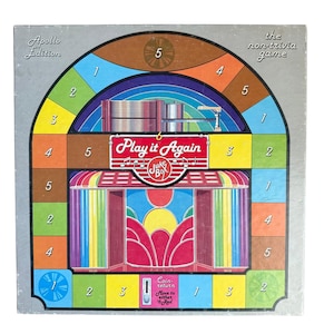 May include: A square board game box titled Play it Again Juke Box Apollo Edition the non-trivia game. The colorful graphic features a jukebox illustration with numbered spaces in green, yellow, orange, and blue surrounding the central image.