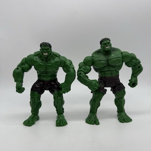 May include: Two green Hulk action figures. Each figure is muscular, with a detailed facial expression and dark shorts. The figures are posed in a stance, ready for action. The figures are made of plastic.