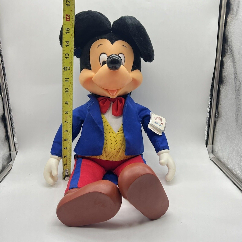 Peut inclure: Une peluche de Mickey Mouse portant un costume bleu avec un gilet jaune et un pantalon rouge. La peluche est assise les jambes crois&eacute;es et porte un n&oelig;ud papillon rouge. La peluche mesure environ 43 cm de haut.