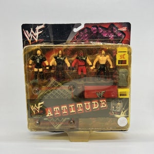 May include: A WWF Attitude action figure set featuring four wrestlers, a wrestling ring, a bin, and a WWF logo. The wrestlers are wearing black and red wrestling attire. The set is packaged in a clear plastic box with a yellow and red background.