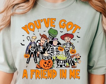 May include: A light blue t-shirt featuring a graphic of the Toy Story characters dressed as skeletons for Halloween. The text "You've Got A Friend In Me" is printed below the characters.