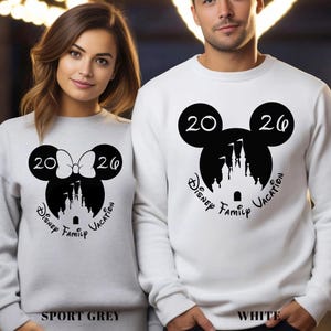 A woman and a man wearing matching white sweatshirts with a Disney-themed design.