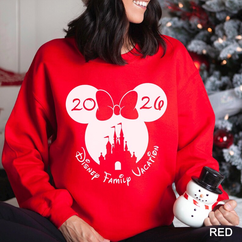 A woman wearing a red sweater with a white Mickey Mouse logo and the text "Disney Family Vacation" is holding a snowman and a mug.