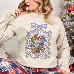 A woman wearing a white sweatshirt with a graphic design featuring cartoon characters and a bow.