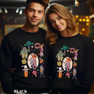 A man and a woman are standing next to each other, both wearing black sweatshirts with colorful cartoon characters and designs.