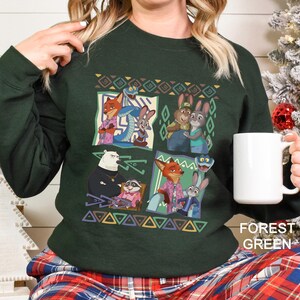 A woman wearing a green sweatshirt with a colorful graphic of cartoon animals, including a polar bear, foxes, and rabbits, along with geometric patterns. She is holding a white mug.