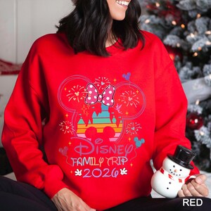 A woman wearing a red sweater with a Disney-themed design and text, holding a snowman toy.