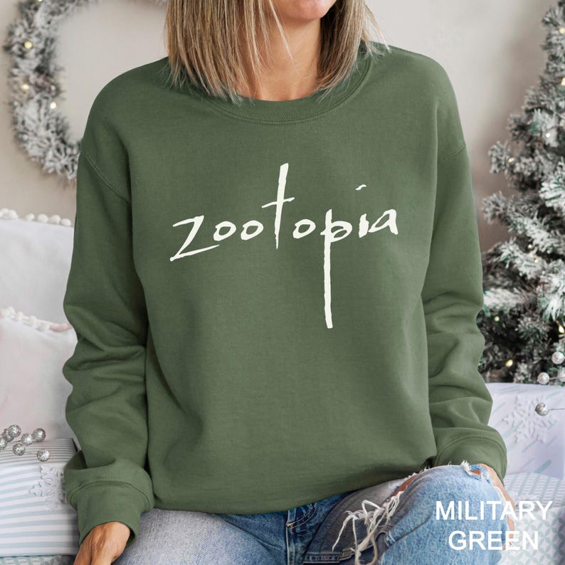 A woman wearing a green sweatshirt with the word "Zootopia" printed on it, sitting in front of a Christmas tree.
