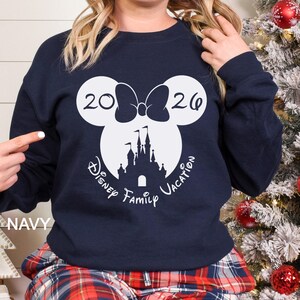 A woman wearing a navy blue sweatshirt with a white graphic design featuring a castle and the text "Disney Family Vacation" printed on it.