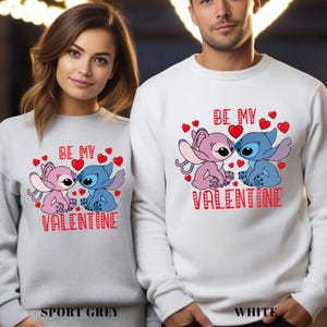 A man and a woman wearing matching white sweatshirts with a Valentine's Day design featuring a cartoon character and the text "Be my Valentine".