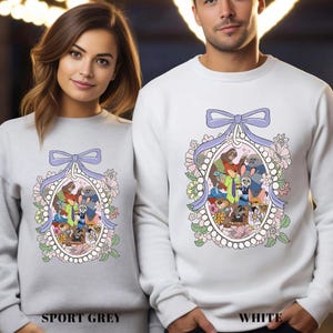 A woman and a man standing side by side, both wearing white sweaters with a colorful graphic design featuring cartoon characters and floral elements.
