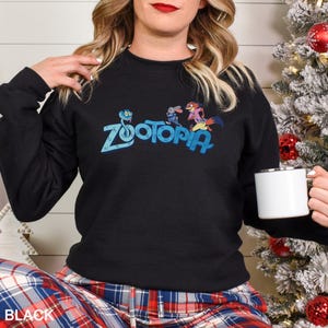 A woman wearing a black sweater with the word "Zootopia" printed on it, holding a white mug, and sitting in front of a Christmas tree.