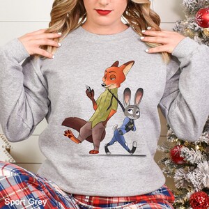 A woman wearing a grey sweatshirt with a cartoon image of a fox and a rabbit on it.