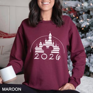 A woman wearing a burgundy sweater with a white graphic design of a castle and the year "2020" printed on it.