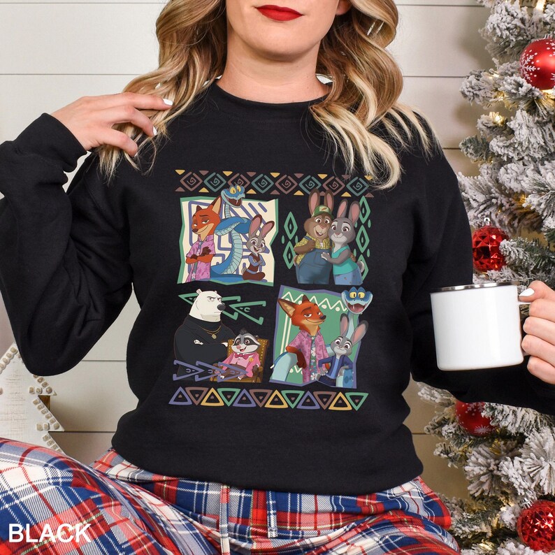 A woman wearing a black sweater with a colorful graphic of cartoon characters is holding a white mug.