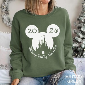 A woman wearing a green sweatshirt with a white graphic of a castle and the text "Disney Family Vacation" printed on it.