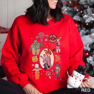 A woman wearing a red sweater with a cartoon character design on it, holding a snowman toy.