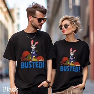 A man and a woman wearing matching black t-shirts with a cartoon rabbit character and the text "BUSTED!" printed on them.